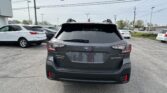 Rear view of a dark gray Subaru Outback in a parking lot with other cars and overhead power lines in a suburban area.