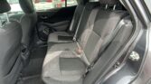 Interior of a car's rear row with three black fabric seats, headrests, and seat belts; view of parked cars outside through the windows.