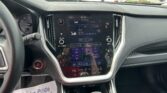 Center touchscreen shows FM radio and climate controls in a modern car, with the steering wheel on the left and a parking lot visible through the windshield.