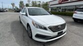 White Hyundai sedan in foreground, parked in a dealership lot in front of an E-Z Loan Auto building with other cars and trees in the background.