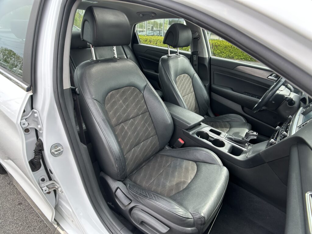 Interior of a car showing black leather front seats, center console, and dashboard with the driver’s door open to the outside.
