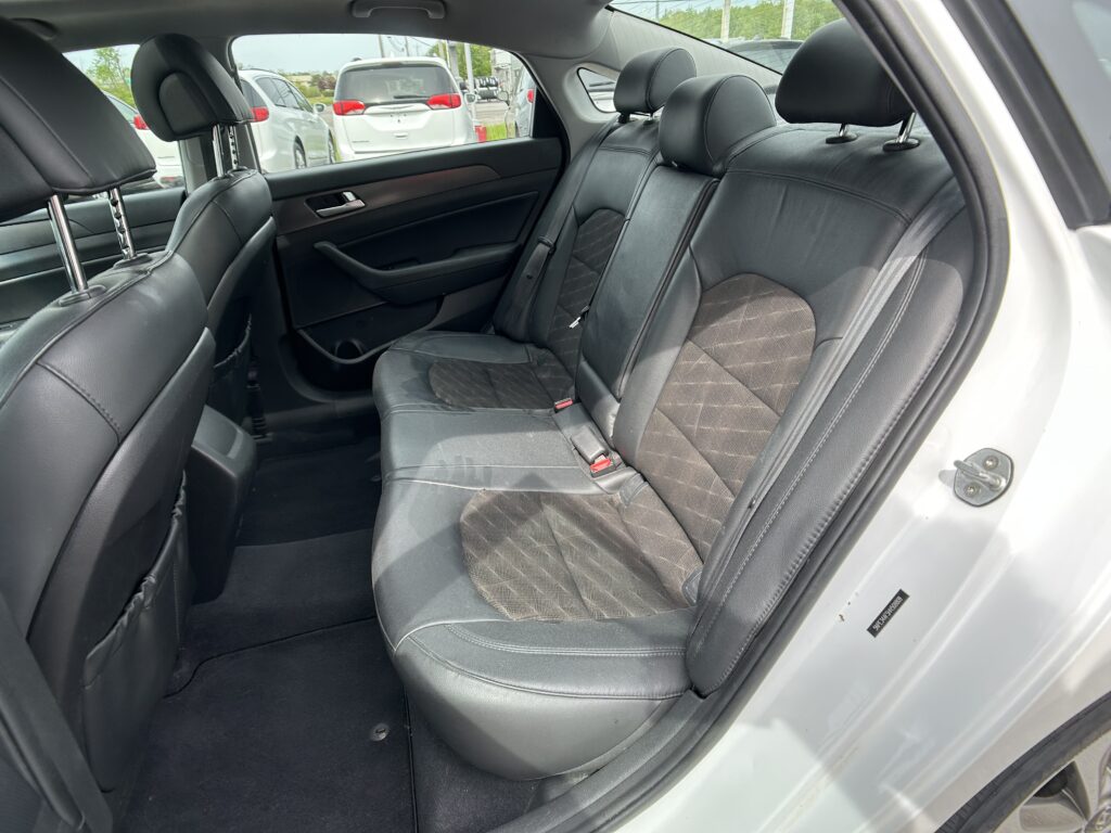 Back seat of a car with black leather seats and headrests, viewed from the rear passenger side window. Reich