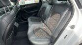 Back seat of a car with black leather seats and headrests, viewed from the rear passenger side window. Reich