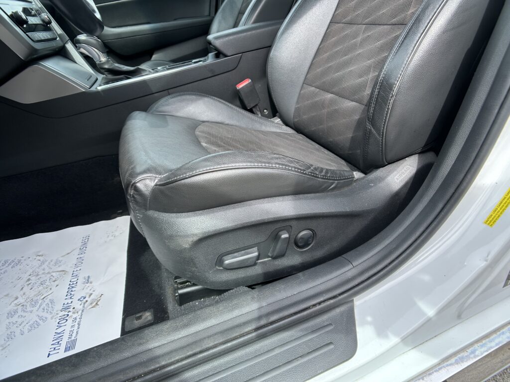 Interior of a car showing the front seats, center console, and gear shifter; black leather upholstery and a red seatbelt buckle visible on the side of the driver seat.