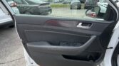 Interior of a car door with window controls, open to a parking lot filled with many parked cars at a dealership.
