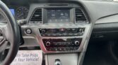 Dashboard interior view showing a large touchscreen display, air vents, and climate controls between the driver and passenger seats, with the gear shifter in the foreground.