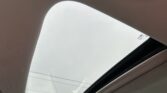 View upward through a car's panoramic sunroof to a cloudy sky, beige headliner framing the opening.