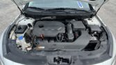 Open car hood revealing engine bay and battery compartment inside a light-colored vehicle.