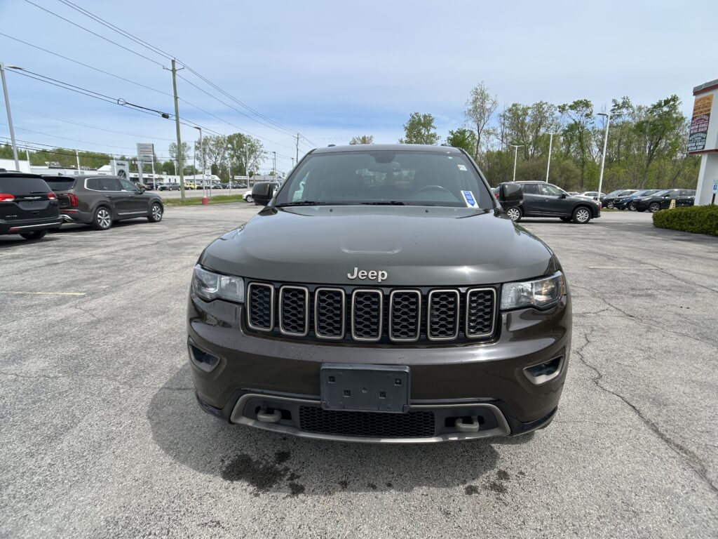 Front view of a gray Jeep SUV in a car dealership lot, with other vehicles and power lines in the background.