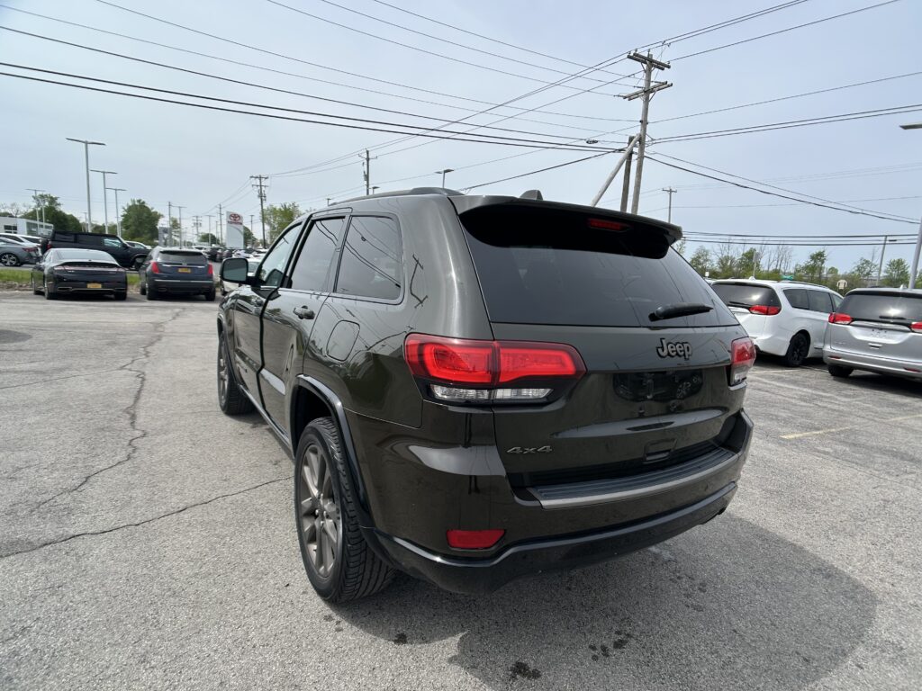 Black Jeep SUV photographed from the rear in a parking lot with other cars and power lines overhead, showing 4x4 badge and red tail lights.