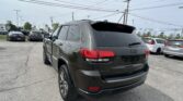 Black Jeep SUV photographed from the rear in a parking lot with other cars and power lines overhead, showing 4x4 badge and red tail lights.