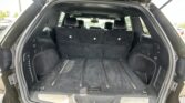 Open SUV trunk with third-row seats upright, showing black cargo area and rear seats visible in a parking lot.