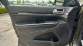 Open-car-door interior: black leather panel with chrome door handle, window/lock controls, and a view of the parking lot outside in the background.