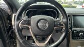Close-up of a Jeep steering wheel inside a car, with the instrument cluster and infotainment display in view.