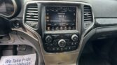 Center console of a car with a touchscreen radio showing Classic Rock 96.9 and climate controls, plus a floor mat that reads 'We Take Pride In Your Vehicle'.