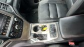 Car interior focused on the center console with the gear shift, cup holders, and leather seats with red stitching.