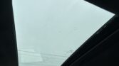 Raindrops on a panoramic sunroof viewed from inside a car, with a pale sky beyond the glass.