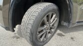 Close-up of a car's front right wheel with a dusty tire and alloy rim inside the wheel well of a dark vehicle.