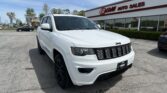 White Jeep SUV in a dealership lot with E-Z LOAN AUTO SALES signage and blue sky behind it.