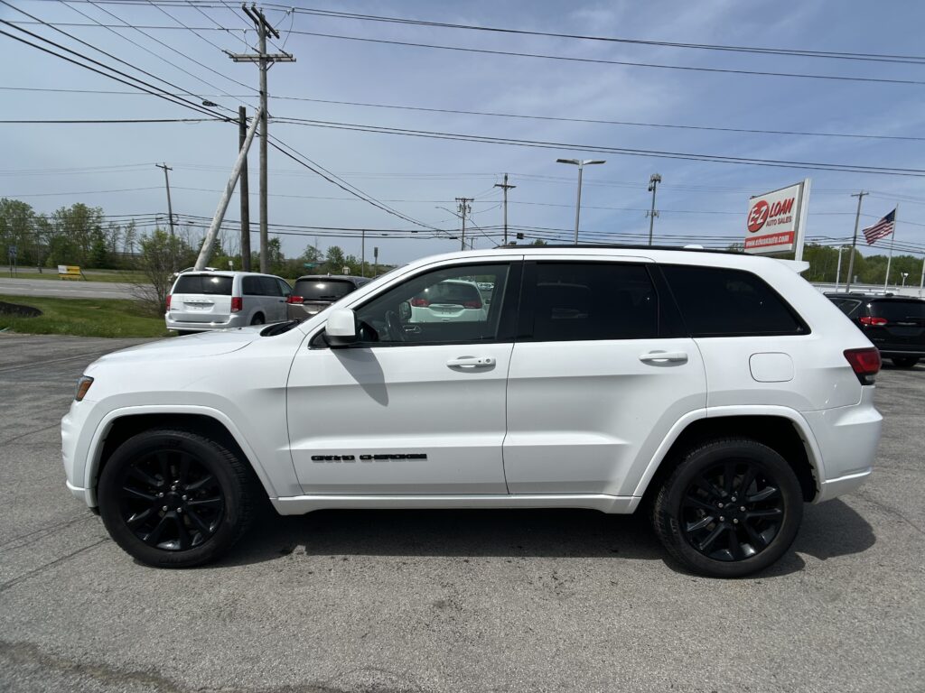 White SUV parked in a dealership lot with other cars and an EZ Auto Sales sign in the background.