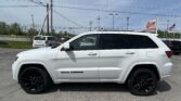 White SUV parked in a dealership lot with other cars and an EZ Auto Sales sign in the background.