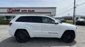 White Jeep Grand Cherokee SUV in the foreground of an auto dealership lot, with 'E-Z LOAN AUTO SALES' building in the background under a clear sky.