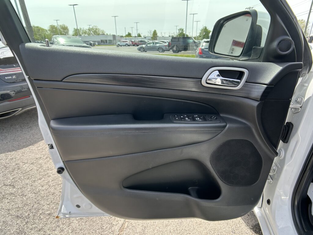 Interior view of a car door panel with a chrome handle and window controls, overlooking a parking lot through the open door