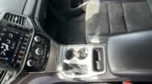 Front interior of a car showing the center console with touchscreen, climate controls, gear shifter, and cup holders beside black leather seats.