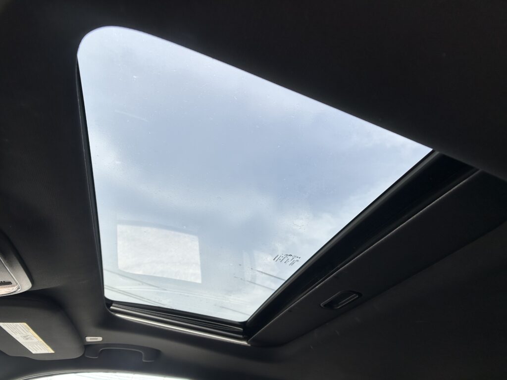 Interior of a car with an open sunroof showing a cloudy sky above.