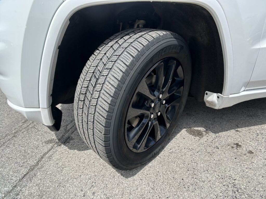 Close-up of a car tire on a black alloy wheel, with the silver vehicle’s wheel well visible behind it.