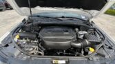 Open hood of a dark SUV revealing the engine bay, with battery on the left and bright yellow coolant cap on the right.