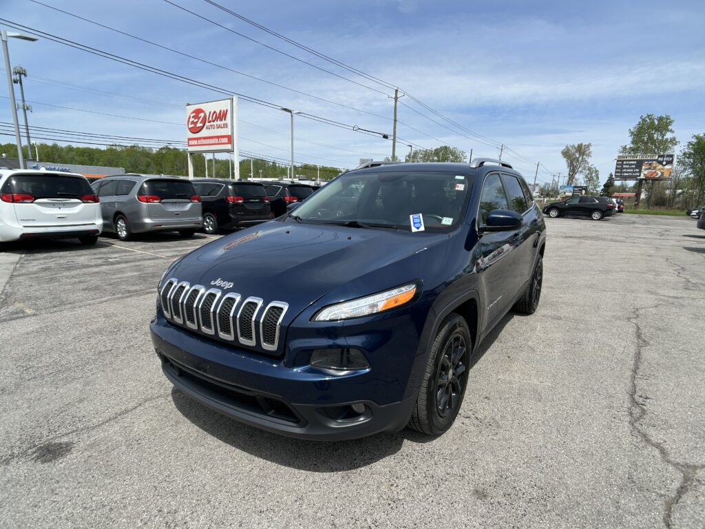 Blue Jeep SUV in the foreground at a car dealership lot, with rows of minivans behind and an EZ Loan Auto Sales sign in the distance.