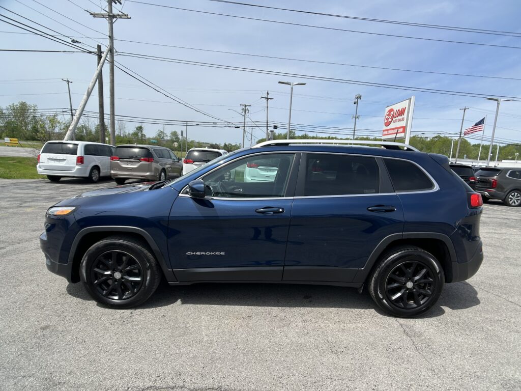 Blue Jeep Grand Cherokee in the foreground of a car dealership lot, with other minivans and an EZ Loan Auto Sales sign in the background.