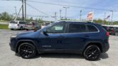 Blue Jeep Grand Cherokee in the foreground of a car dealership lot, with other minivans and an EZ Loan Auto Sales sign in the background.