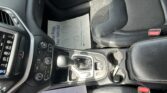 Front passenger area of a car: black leather seats, center console, gear shifter, and a paper mat on the floor with blue text partially visible inside the vehicle.