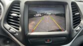 Rearview camera display showing parking lot view with green/yellow/red guides and the text 'Check Entire Surroundings' at the top, inside a car dashboard.