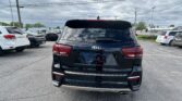 Rear view of a black Kia SUV in a busy parking lot with other cars and a cloudy sky above, showing taillights and Kia emblem on the hatch.
