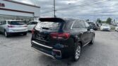 Black Kia SUV in the foreground at a car dealership lot with rows of vehicles and a white building behind it.