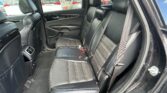 Rear row of a black leather SUV interior with visible seat belts and headrests, door panel, and outside parked cars through the windows