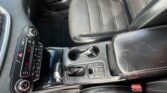 Interior of a car showing the center console with gear shifter, cup holder, and climate controls surrounded by black leather seats with white stitching.