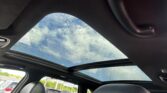 Looking up through the car's panoramic sunroof at a blue sky with raindrops on the glass from inside the vehicle