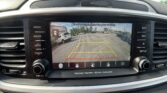 Car infotainment screen showing a rearview camera feed with parking guide lines and the safety message 'Checks surroundings for your safety'.