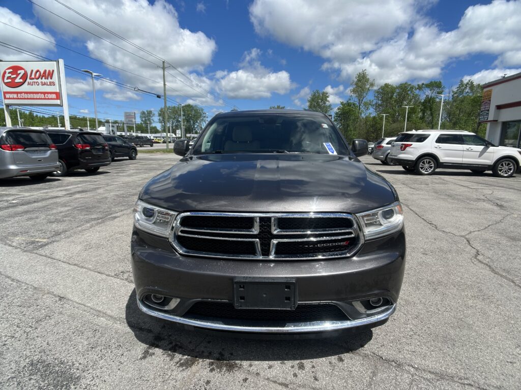 Front view of a dark gray Dodge SUV in a parking lot, with a dealership sign reading 'E-Z LOAN Auto Sales' on the left and blue sky with clouds above.