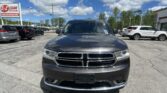 Front view of a dark gray Dodge SUV in a parking lot, with a dealership sign reading 'E-Z LOAN Auto Sales' on the left and blue sky with clouds above.