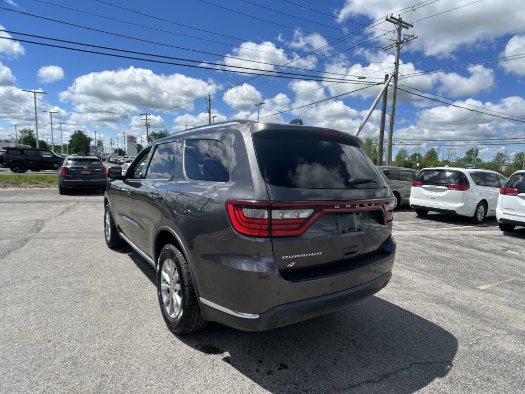 Rear of a gray Dodge Durango in a parking lot with other cars and power lines overhead against a blue sky with clouds.