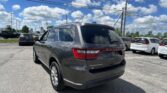 Rear of a gray Dodge Durango in a parking lot with other cars and power lines overhead against a blue sky with clouds.