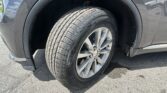Close-up of a car's front wheel and tire, showing the tread and silver alloy rim, with the wheel well and fender nearby on an asphalt surface.