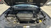 Open car hood over the engine bay; V6 engine cover visible, battery on left, various hoses.