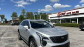 Silver Cadillac SUV parked in a dealership lot in front of EZ Loan Auto Sales, blue sky with fluffy clouds above.