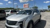 Silver Cadillac SUV parked in a car lot under a bright blue sky with scattered white clouds and an E-Z LOAN Auto Sales sign in the background